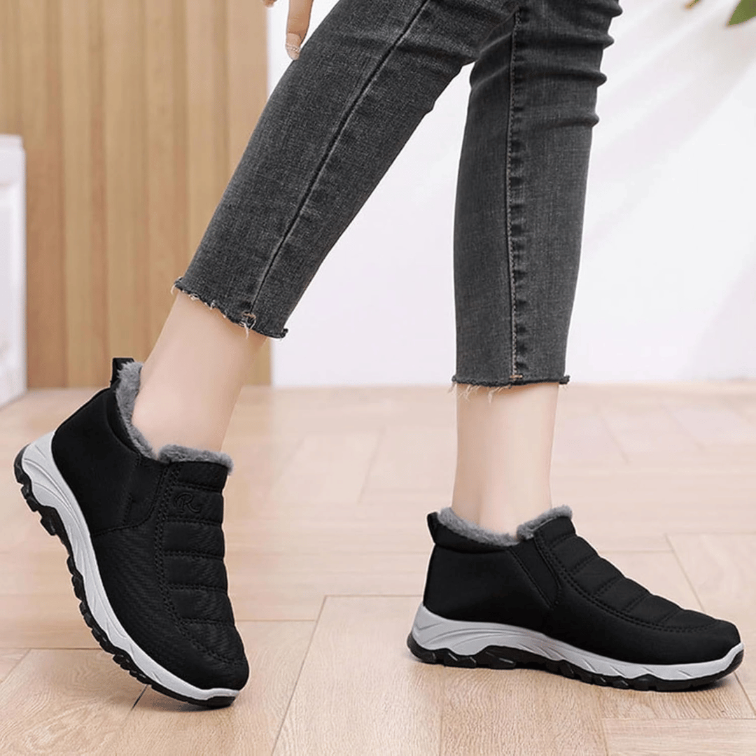 A pair of black orthopedic women's ankle booties with a fur lining at the top, worn by a person with jeans.